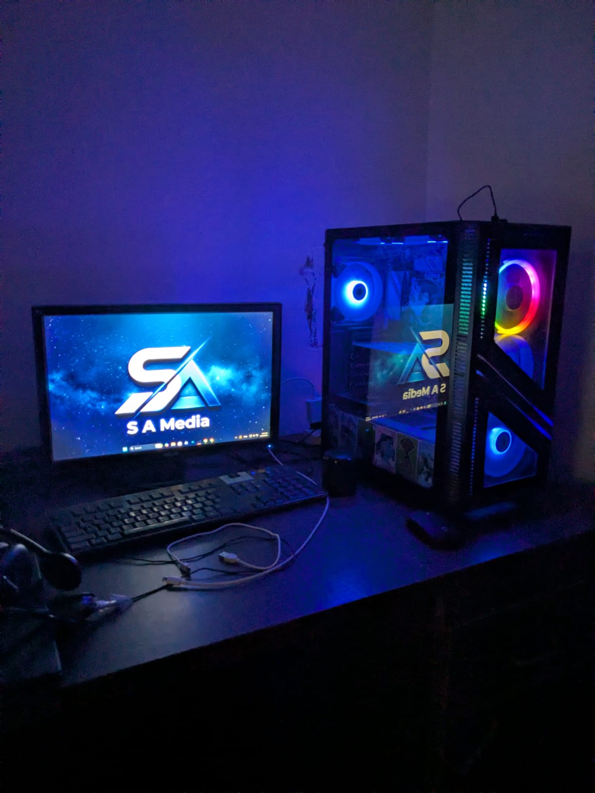 S A Media build workspace with monitor displaying the SA Media logo, keyboard and an RGB-lit PC tower