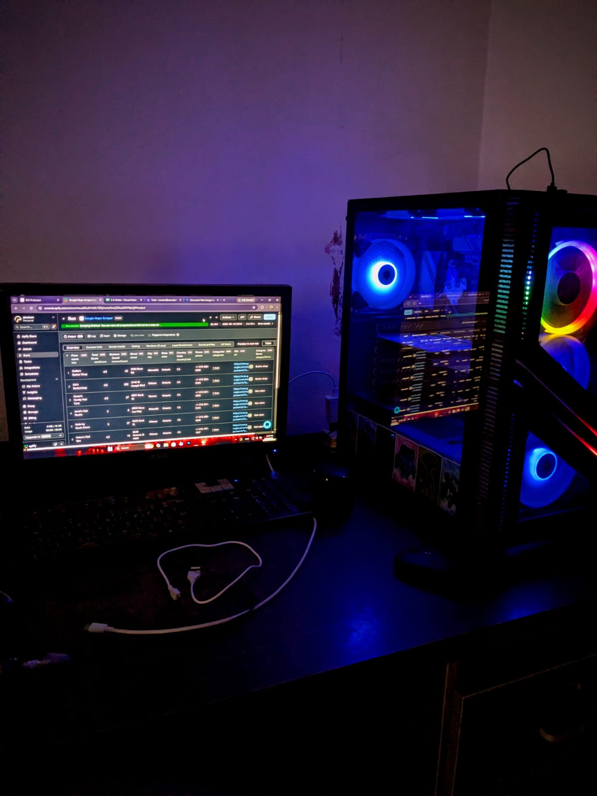 S A Media build desk showing a monitor with a Google Maps Scraper data dashboard beside an RGB-lit PC tower in a dim room